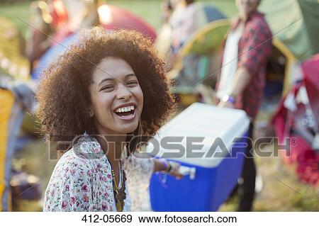 Portrait of laughing woman helping man carry cooler outside tents at music festival View Large Photo Image Stock Photo - Portrait of laughing woman helping man carry cooler outside tents at music festival. Fotosearch