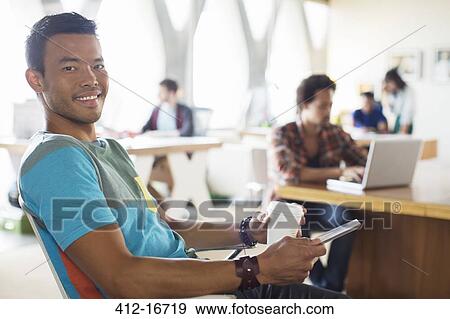 Stock Photo - Portrait of smiling casual businessman drinking coffee and using digital tablet in office. Fotosearch