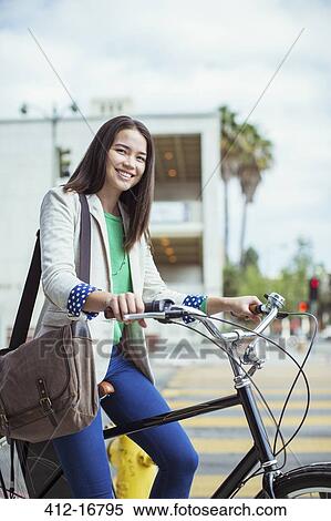 Stock Photography - Portrait of smiling casual businesswoman on bicycle on urban street. Fotosearch
