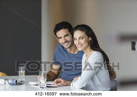 Stock Photo - Portrait of smiling couple paying bills at table. Fotosearch