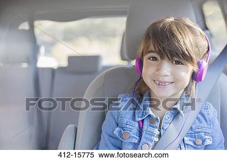 Stock Photography - Portrait of smiling girl with headphones in back seat of car. Fotosearch