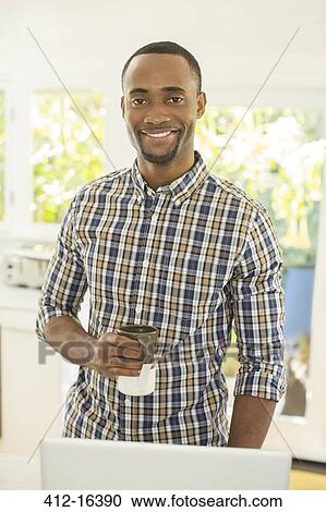 Stock Image - Portrait of smiling man drinking coffee at laptop. Fotosearch