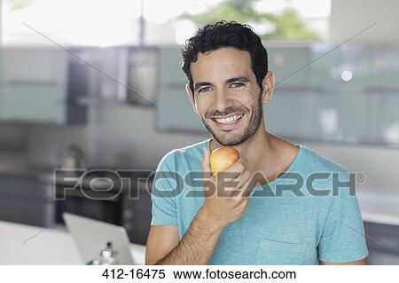 Portrait of smiling man eating apple in kitchen View Large Photo Image Stock Photography - Portrait of smiling man eating apple in kitchen. Fotosearch