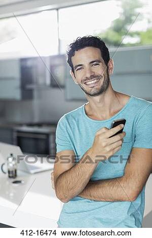 Portrait of smiling man with cell phone in kitchen View Large Photo Image Picture - Portrait of smiling man with cell phone in kitchen. Fotosearch