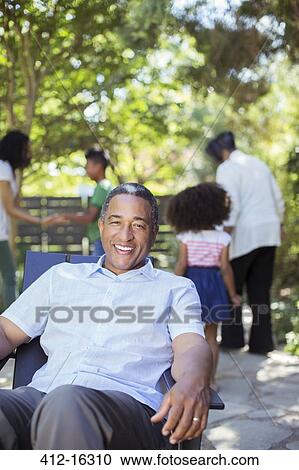 Portrait of smiling senior man on patio with family in background View Large Photo Image Stock Image - Portrait of smiling senior man on patio with family in background. Fotosearch