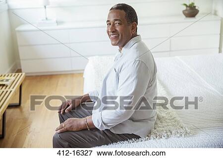 Stock Photo - Portrait of smiling senior man sitting at the edge of bed. Fotosearch