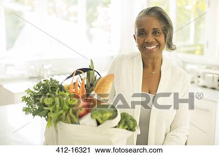 Portrait of smiling senior woman with groceries in kitchen View Large Photo Image Stock Image - Portrait of smiling senior woman with groceries in kitchen. Fotosearch
