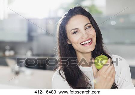 Portrait of smiling woman eating apple in kitchen View Large Photo Image Stock Image - Portrait of smiling woman eating apple in kitchen. Fotosearch