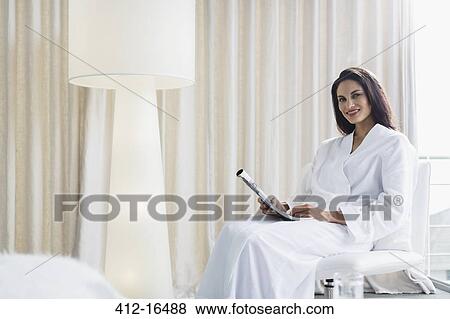 Stock Photo - Portrait of smiling woman in bathrobe reading newspaper. Fotosearch