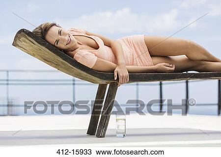 Stock Image - Portrait of smiling woman laying on lounge chair. Fotosearch