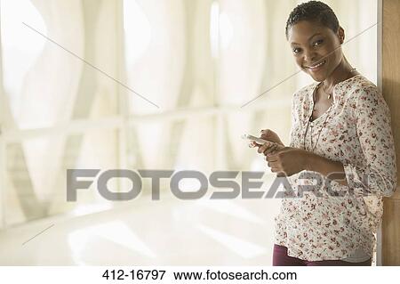 Portrait of smiling woman text messaging with cell phone in sunny corridor View Large Photo Image Stock Photo - Portrait of smiling woman text messaging with cell phone in sunny corridor. Fotosearch