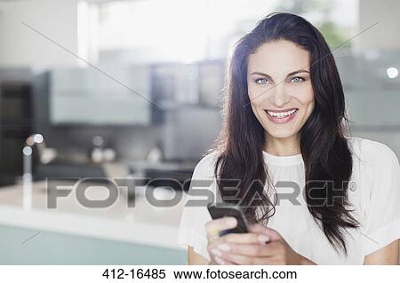 Portrait of smiling woman texting with cell phone in kitchen View Large Photo Image Stock Photography - Portrait of smiling woman texting with cell phone in kitchen. Fotosearch