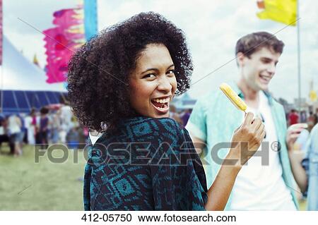 Stock Image - Portrait of woman eating flavored ice at music festival. Fotosearch