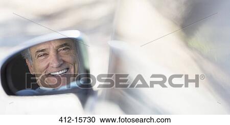 Stock Image - Reflection of smiling senior man in side-view car mirror. Fotosearch
