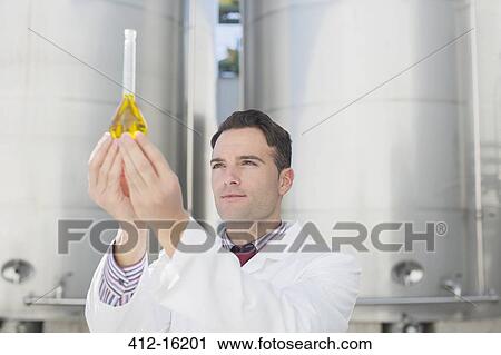 Stock Image - Scientist examining liquid in beaker next to silage storage towers. Fotosearch