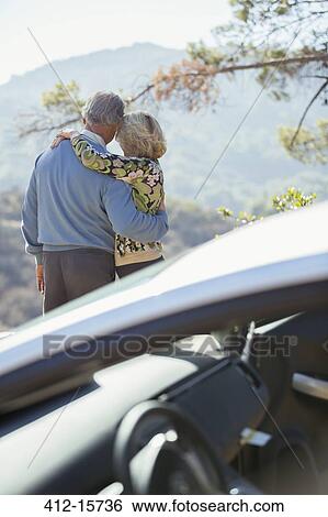 Stock Photograph - Senior couple looking at mountain view outside car. Fotosearch