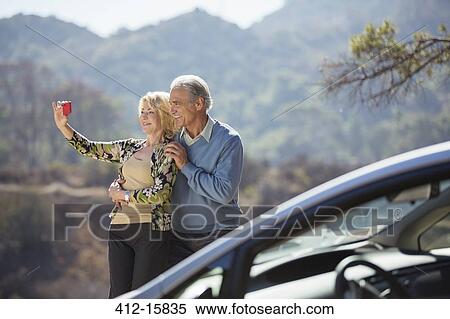 Senior couple taking self-portrait at roadside outside car View Large Photo Image Stock Photography - Senior couple taking self-portrait at roadside outside car. Fotosearch