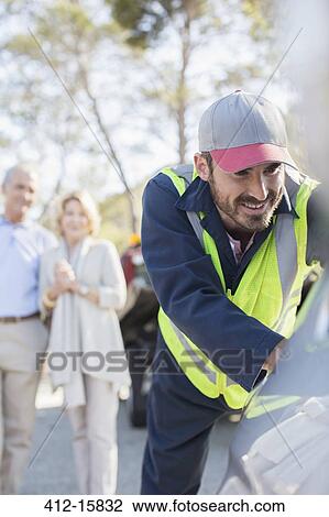 Stock Image - Senior couple watching roadside mechanic push car. Fotosearch