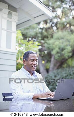 Stock Image - Senior man using laptop at patio table. Fotosearch