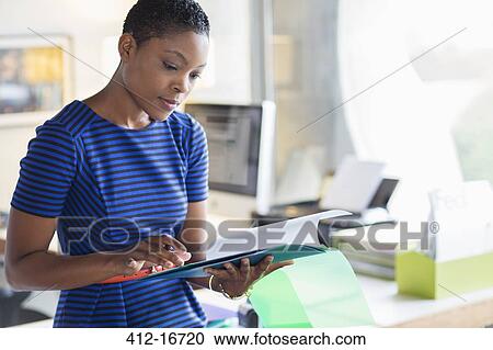 Stock Image - Serious businesswoman reviewing paperwork in office. Fotosearch