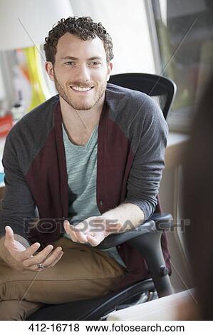 Stock Photo - Smiling casual businessman gesturing in office. Fotosearch