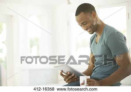 Stock Photo - Smiling man drinking coffee and using digital tablet. Fotosearch