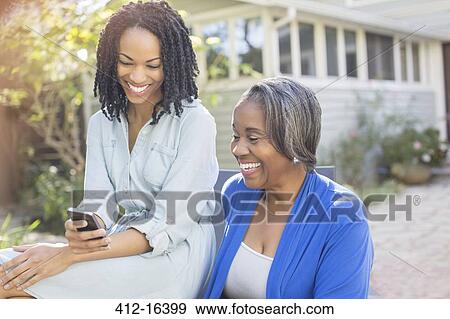 Smiling mother and daughter text messaging with cell phone on patio View Large Photo Image Stock Photo - Smiling mother and daughter text messaging with cell phone on patio. Fotosearch