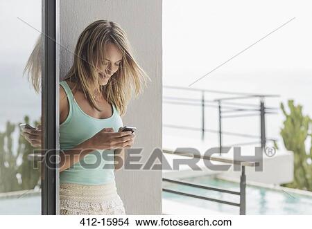 Picture - Smiling woman texting with cell phone on patio. Fotosearch