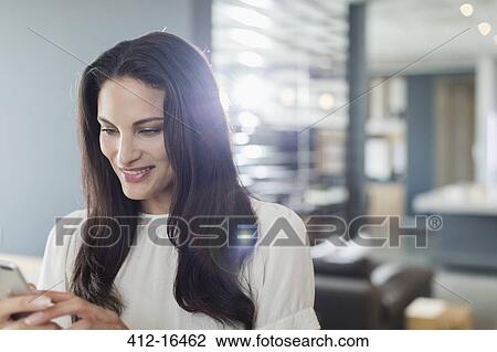 Stock Image - Smiling woman texting with cell phone at home. Fotosearch