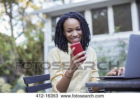 Smiling woman using cell phone and laptop on patio View Large Photo Image Stock Image - Smiling woman using cell phone and laptop on patio. Fotosearch