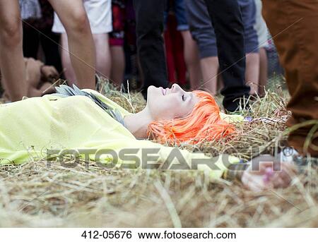 Stock Photograph - Woman in wig laying with arms outstretched in grass at music festival. Fotosearch