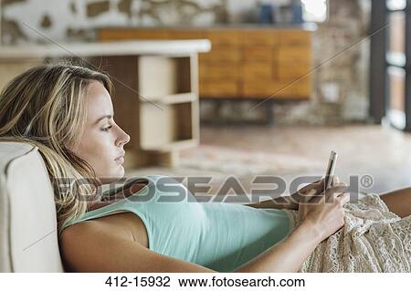 Stock Image - Woman laying on sofa and texting with cell phone. Fotosearch