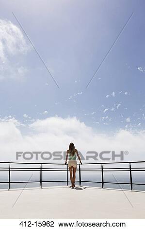 Woman standing on balcony overlooking ocean View Large Photo Image Stock Image - Woman standing on balcony overlooking ocean. Fotosearch