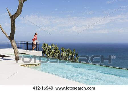 Woman standing on poolside balcony overlooking ocean View Large Photo Image Stock Photo - Woman standing on poolside balcony overlooking ocean. Fotosearch