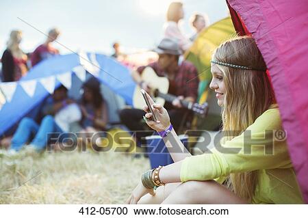 Stock Image - Woman text messaging with cell phone at tent at music festival. Fotosearch
