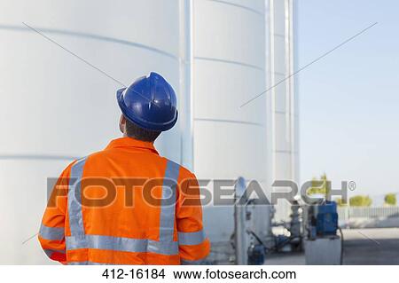 Picture - Worker looking up at silage storage towers. Fotosearch
