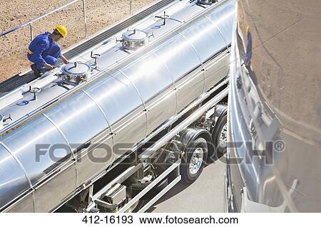 Stock Image - Worker on platform above stainless steel milk tanker. Fotosearch