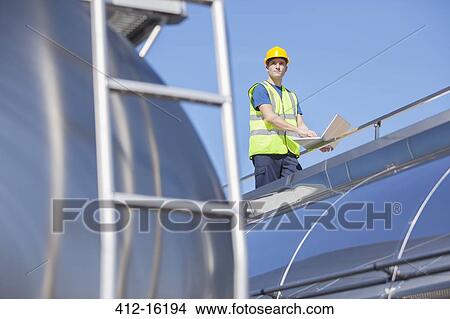 Worker using laptop on platform above stainless steel milk tanker View Large Photo Image Picture - Worker using laptop on platform above stainless steel milk tanker. Fotosearch