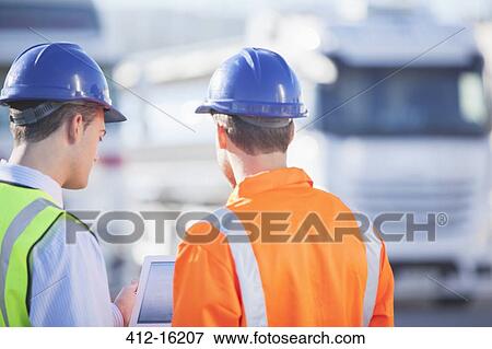 Workers using digital tablet near commercial trucks View Large Photo Image Stock Photo - Workers using digital tablet near commercial trucks. Fotosearch