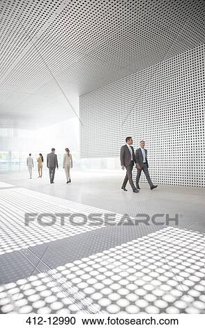 Stock Image - Business people walking in modern courtyard. Fotosearch