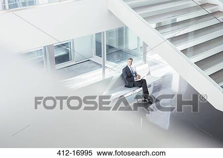 Businessman sitting in modern lobby View Large Photo Image Stock Photography - Businessman sitting in modern lobby. Fotosearch