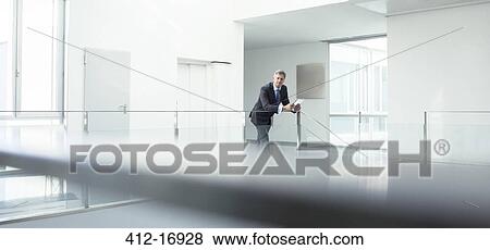 Stock Photo - Businessman standing at railing in office. Fotosearch