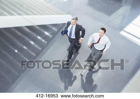 Stock Image - Businessmen with suitcases running in lobby. Fotosearch