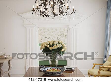Stock Photograph - Chandelier above rose bouquet on table in luxury foyer. Fotosearch