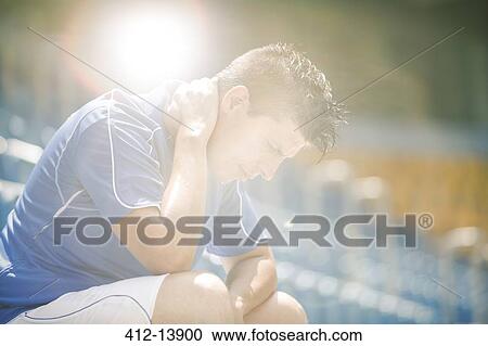 Stock Image - Disappointed soccer player sitting in stadium. Fotosearch
