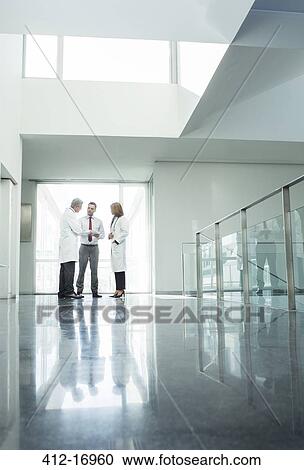 Stock Image - Doctors and administrators talking in hospital corridor. Fotosearch