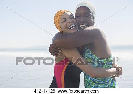 Stock Photograph - Enthusiastic women hugging in bathing suits and caps. Fotosearch