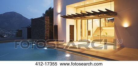 Stock Photography - Illuminated modern house overlooking swimming pool. Fotosearch