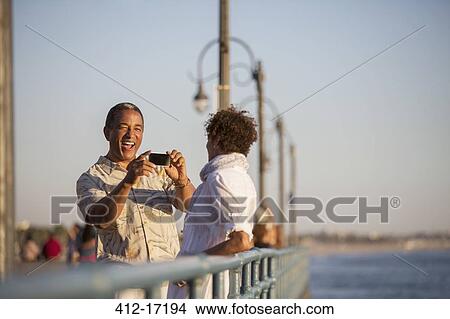 Picture - Man photographing woman on pier. Fotosearch