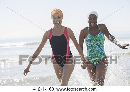 Stock Image - Playful lesbian couple splashing in ocean surf. Fotosearch